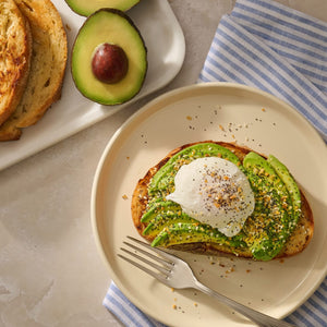A slice of toasted sourdough topped with sliced avocado and a poached egg is generously sprinkled with Mccormick Everything Bagel Seasoning Assorted Form 4.8 Oz.