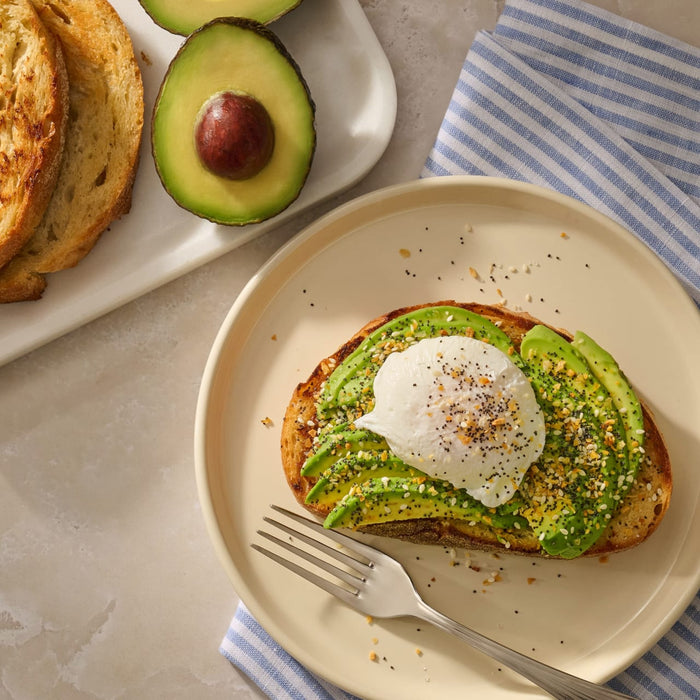 A slice of toasted sourdough topped with sliced avocado and a poached egg is generously sprinkled with Mccormick Everything Bagel Seasoning Assorted Form 4.8 Oz.