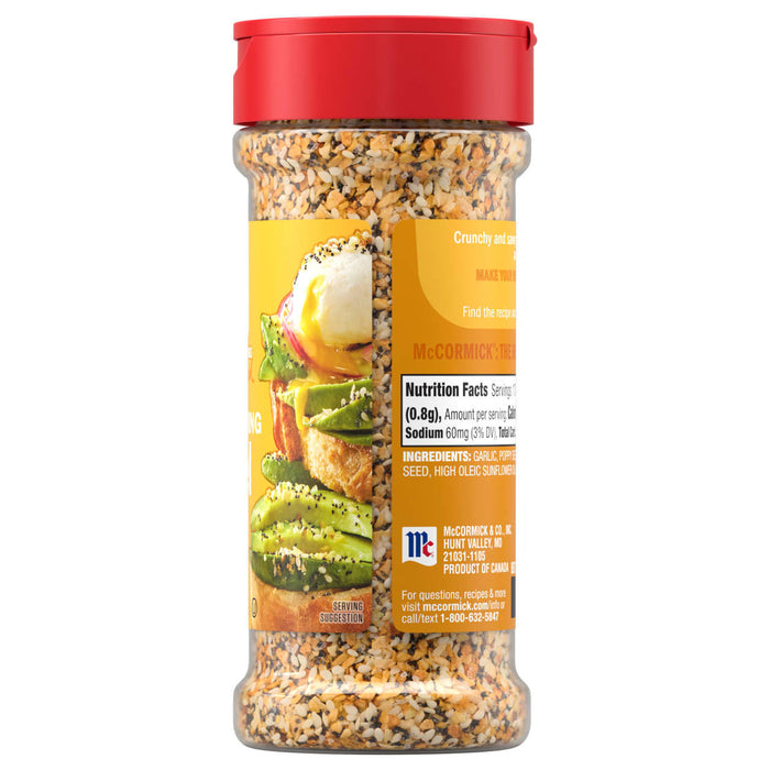 A side view of a clear bottle of Mccormick Everything Bagel Seasoning Assorted Form 4.8 Oz, showing the nutrition facts, ingredients, and a serving suggestion of the seasoning on avocado toast.