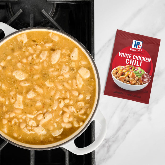 A pot of white chicken chili simmers on a stovetop next to a packet of McCormick White Chicken Chili seasoning mix.