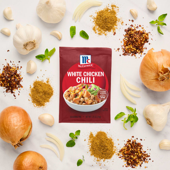 A packet of McCormick's Chicken Chili seasoning mix is surrounded by fresh ingredients like garlic, onions, herbs, and spices.