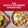A bowl of South of the Border Chicken Chili is shown with toppings like sour cream, avocado, and cheese, alongside lime wedges.