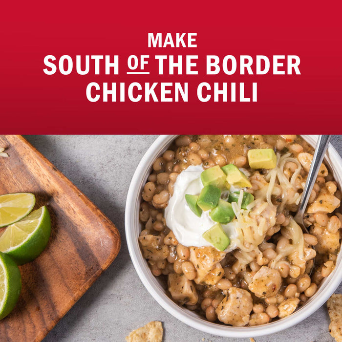A bowl of South of the Border Chicken Chili is shown with toppings like sour cream, avocado, and cheese, alongside lime wedges.