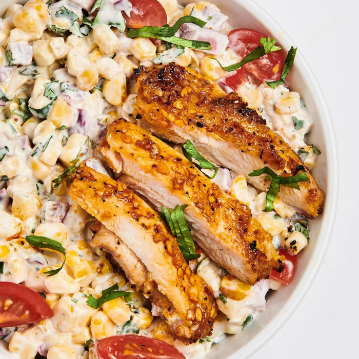 A bowl of corn salad with grilled chicken and tomatoes.