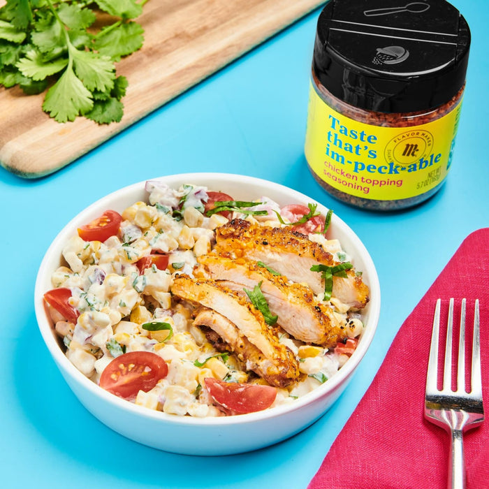 A bowl of corn salad with grilled chicken topped with Flavor Maker's im-peckable chicken topping seasoning.