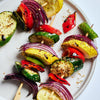 Grilled vegetables on skewers, including zucchini, red pepper, yellow squash, and red onion.