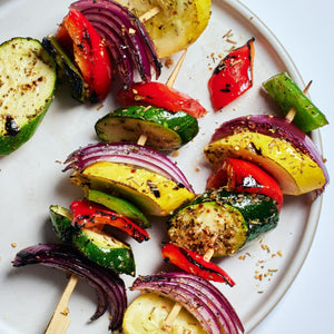 Grilled vegetables on skewers, including zucchini, red pepper, yellow squash, and red onion.