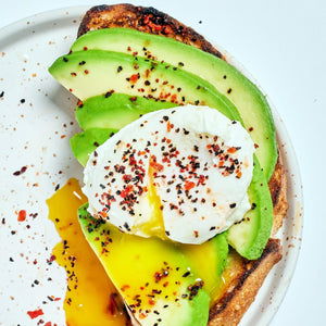 A close-up of avocado toast with a poached egg and red pepper flakes.