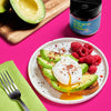 A plate of avocado toast topped with a poached egg and raspberries, with a jar of You Guac to be Kidding avocado topping seasoning.