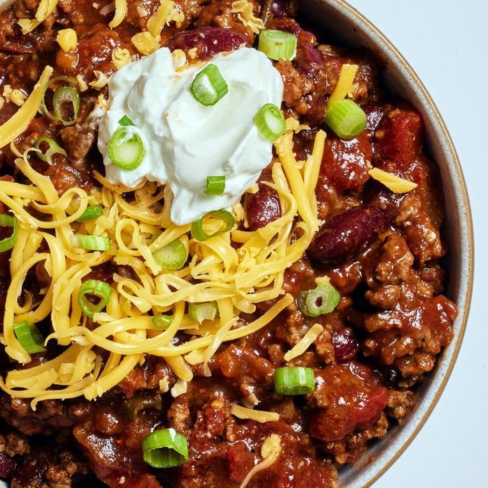 A bowl of chili topped with shredded cheese, sour cream, and green onions.