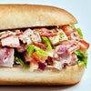 A close-up of a sub sandwich with ham, salami, tomato, lettuce, and red onion.