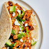 A close-up of a chicken taco with avocado, feta cheese, and lettuce.