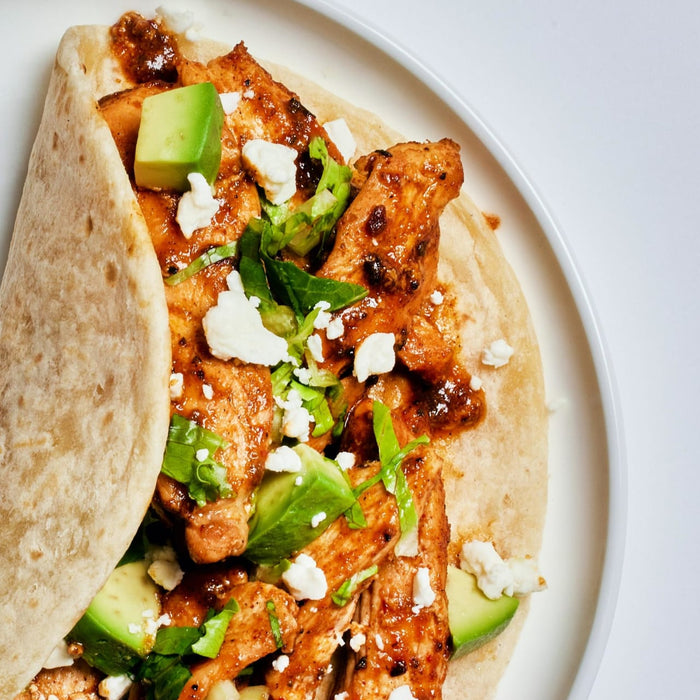 A close-up of a chicken taco with avocado, feta cheese, and lettuce.
