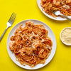 Two plates of shrimp spaghetti with tomato sauce and parmesan cheese are displayed on a vibrant yellow background accompanied by a fork and a bowl of grated cheese.