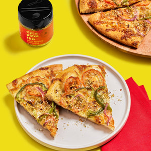 A jar of Get a Pizza This pizza topping seasoning next to two slices of pizza on a white plate.