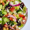 A close-up of a fresh salad with chickpeas, tomatoes, cucumbers, red onion, feta cheese, and lettuce.