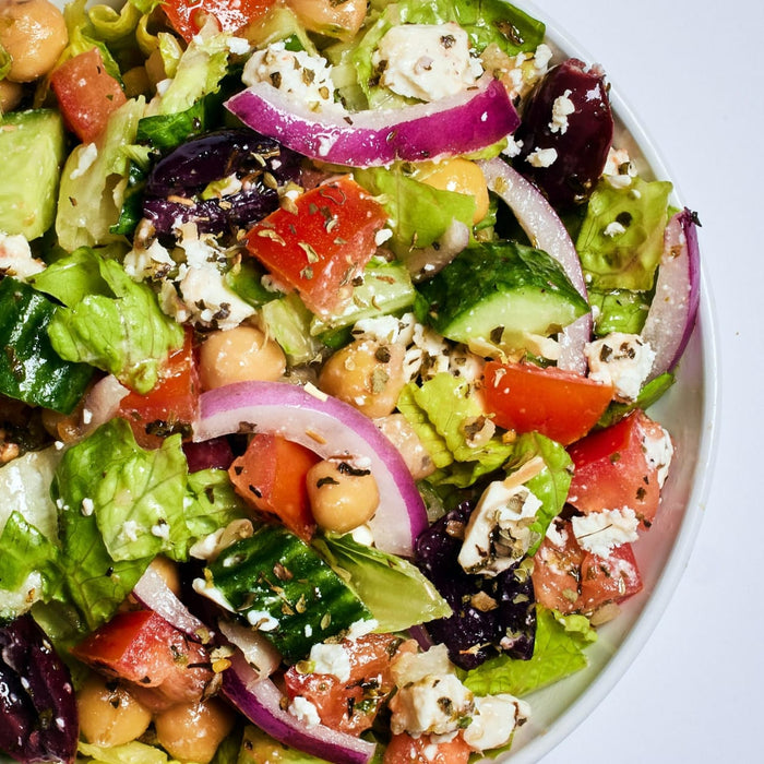 A close-up of a fresh salad with chickpeas, tomatoes, cucumbers, red onion, feta cheese, and lettuce.