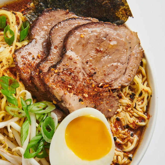 A bowl of ramen with pork, noodles, green onions, bean sprouts, and a soft-boiled egg.