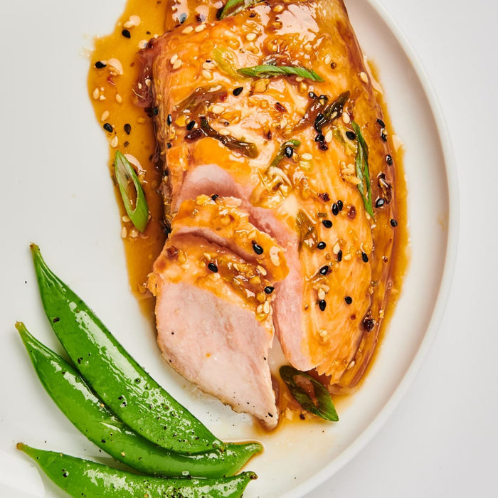 A plate of glazed chicken with sesame seeds and green onions, served with green beans.