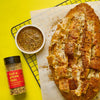 A loaf of cheesy pull-apart bread with a bowl of dipping sauce and a bottle of Flavor Maker Get a pizza this pizza topping seasoning are displayed on a yellow background.