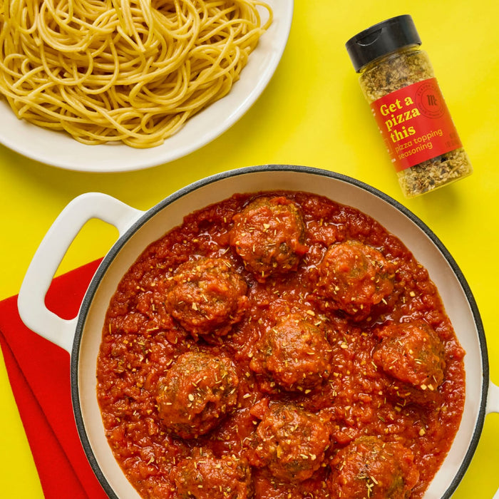 A plate of spaghetti a pot of meatballs in tomato sauce and a bottle of McCormick Get a Pizza This pizza topping seasoning are arranged on a yellow background.