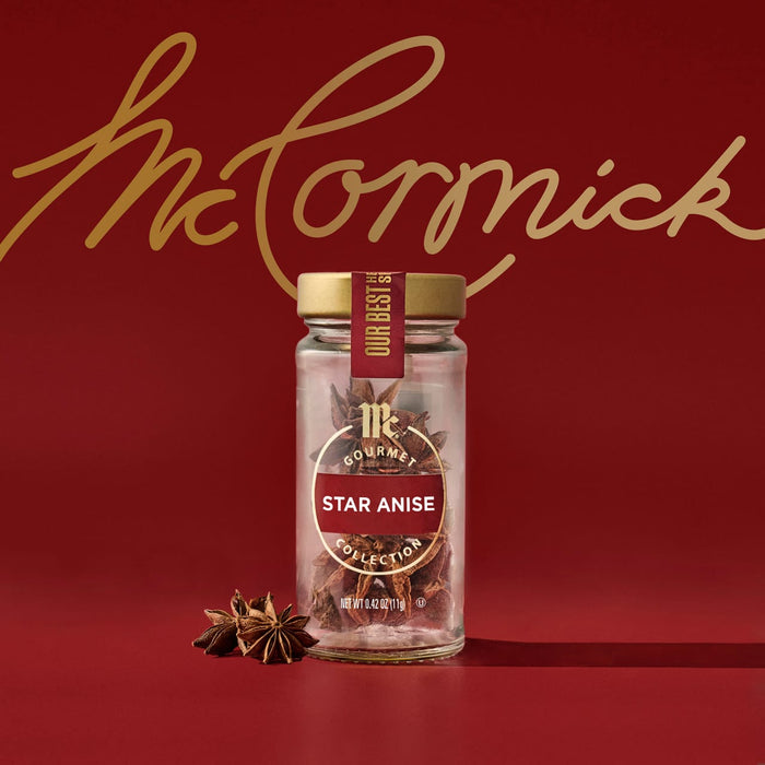 A glass jar of Mccormick Gourmet, 0.42 Oz Star Anise from the Gourmet Collection is displayed against a rich red background featuring the gold McCormick logo, with a few star anise pods resting beside the jar.