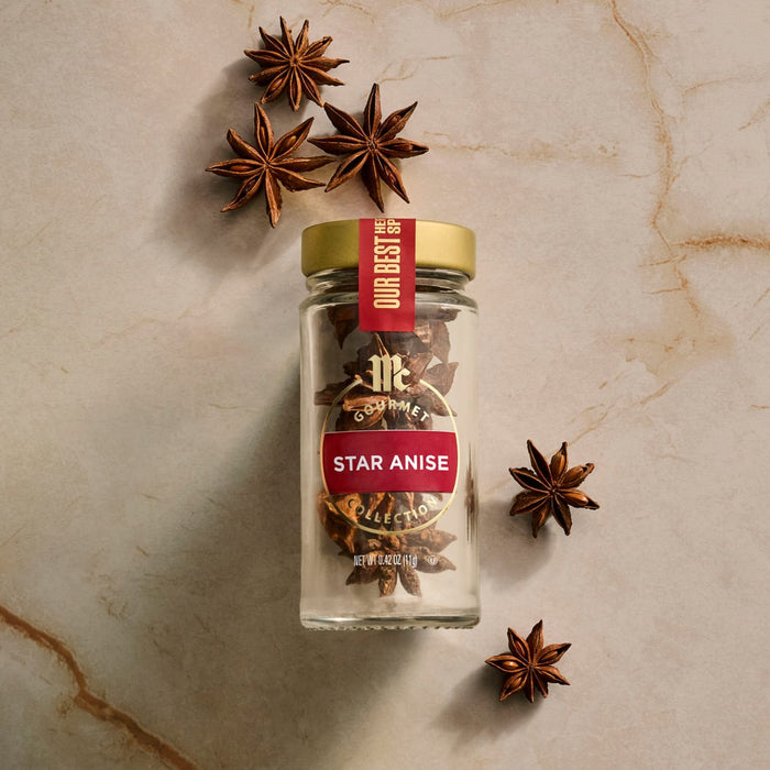 A glass jar of Mccormick Gourmet, 0.42 Oz Star Anise is displayed on a marbled surface, with several whole star anise pods artfully arranged around the bottle.