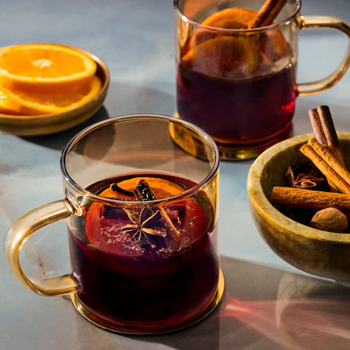 Two inviting mugs of mulled wine are garnished with orange slices and whole spices, including a star anise from a package of Mccormick Gourmet, 0.42 Oz, to create a warm and festive beverage.