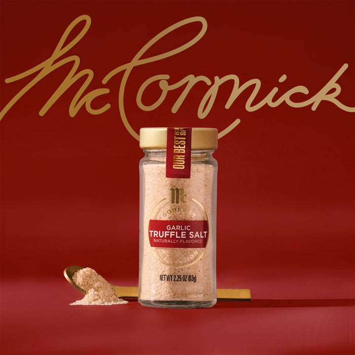 A glass jar of Mccormick Gourmet Garlic Truffle Salt, 2.25 Oz, is centered in a product shot against a rich red background, with a small golden spoon holding a sample of the salt next to the jar.