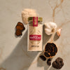 A flat lay photograph shows a jar of Mccormick Gourmet Garlic Truffle Salt, 2.25 Oz, artfully arranged on a marble surface with its key ingredients: fresh garlic, black garlic, and whole and sliced black truffles.