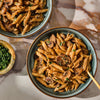 Two bowls of creamy mushroom penne pasta, seasoned with Mccormick Gourmet Garlic Truffle Salt, 2.25 Oz, are served on a marble tabletop with a side of fresh parsley.