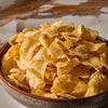 A close-up shot shows a rustic ceramic bowl overflowing with golden potato chips, which have been seasoned with Mccormick Gourmet Garlic Truffle Salt, 2.25 Oz.