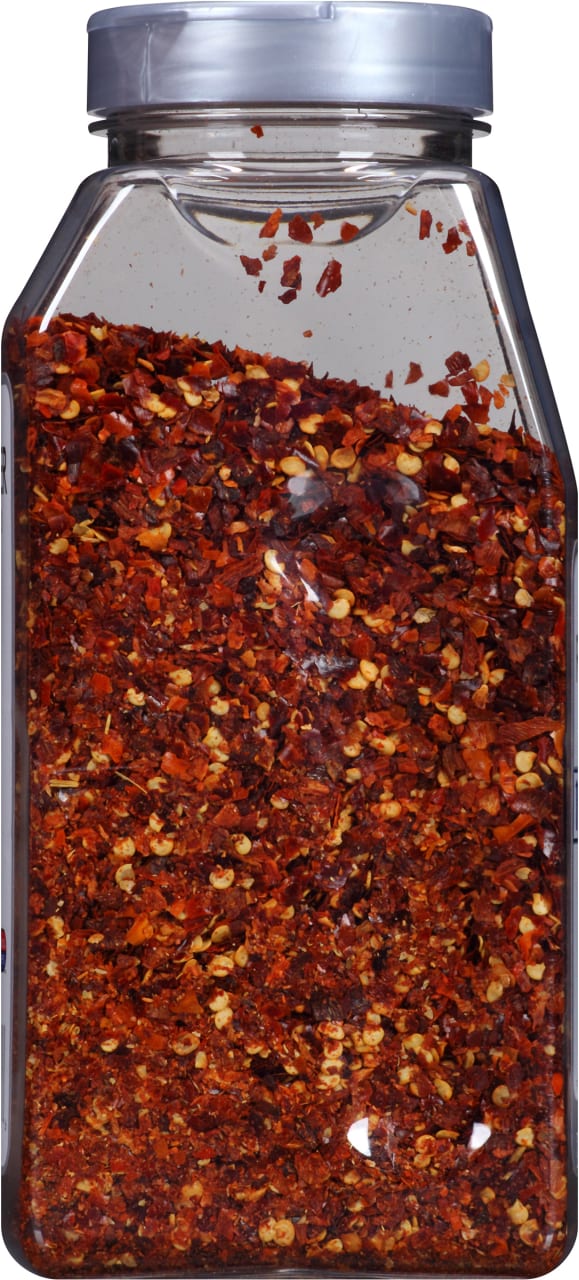 A clear plastic jar filled with crushed red pepper flakes.