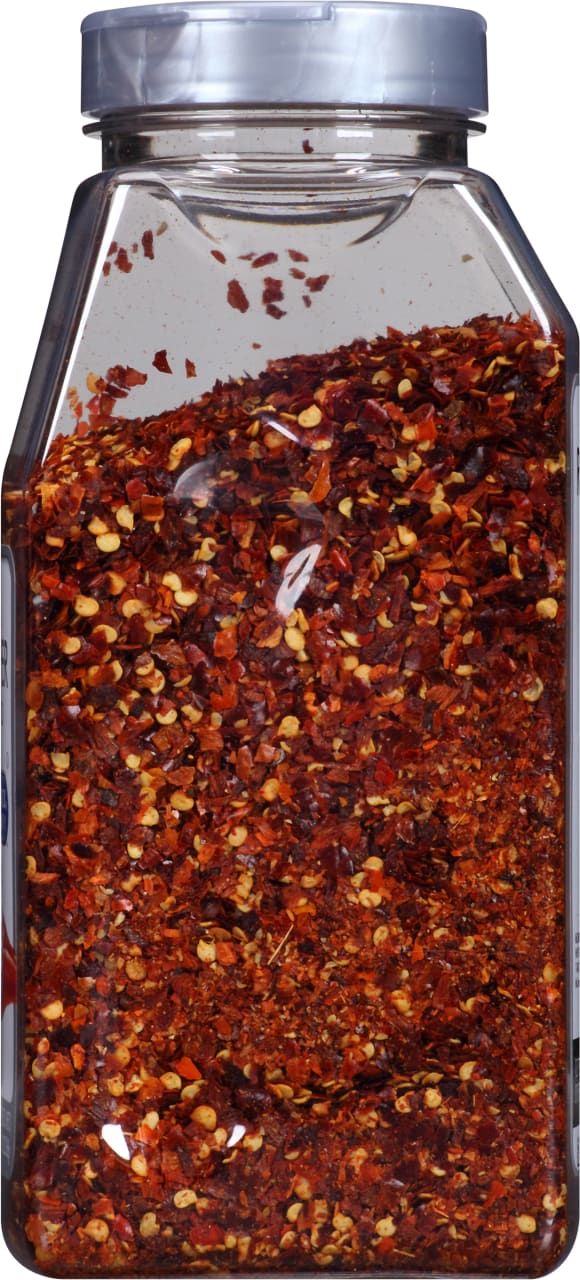 A clear plastic jar filled with red pepper flakes.