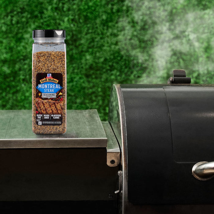 A container of Montreal Steak Spice sits next to a smoking grill, suggesting its use in outdoor cooking.