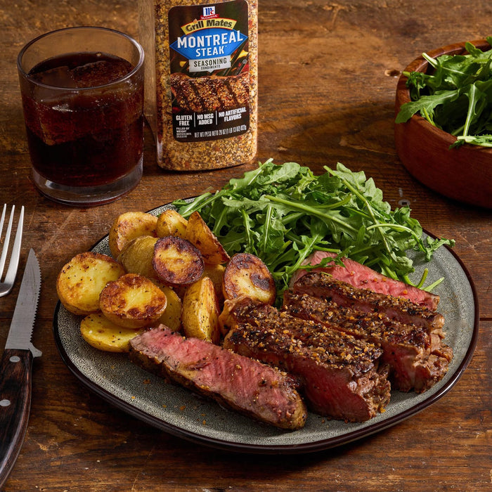 A plate of steak seasoned with McCormick Montreal Steak Seasoning, served with potatoes and greens, alongside a drink.