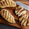 Grilled chicken breasts are sliced on a wooden cutting board.