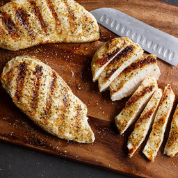 Grilled chicken breasts are sliced on a wooden cutting board.