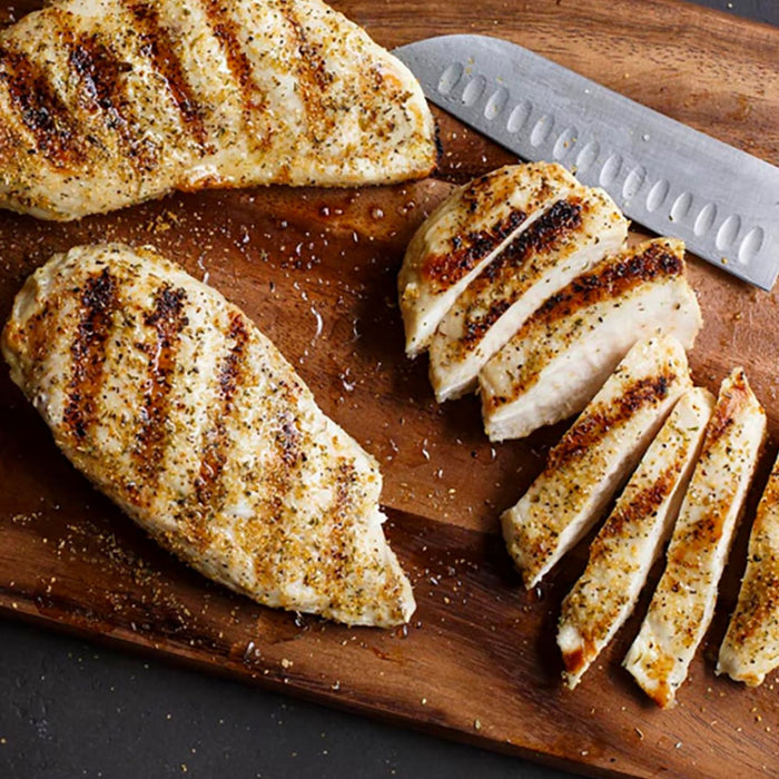 Grilled chicken breasts are sliced on a wooden cutting board.