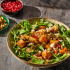 A vibrant salad featuring roasted butternut squash, arugula, pomegranate seeds, and toasted seeds, showcasing a healthy and colorful meal option.