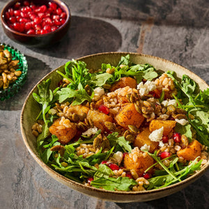 A vibrant salad featuring roasted butternut squash, arugula, pomegranate seeds, and toasted seeds, showcasing a healthy and colorful meal option.