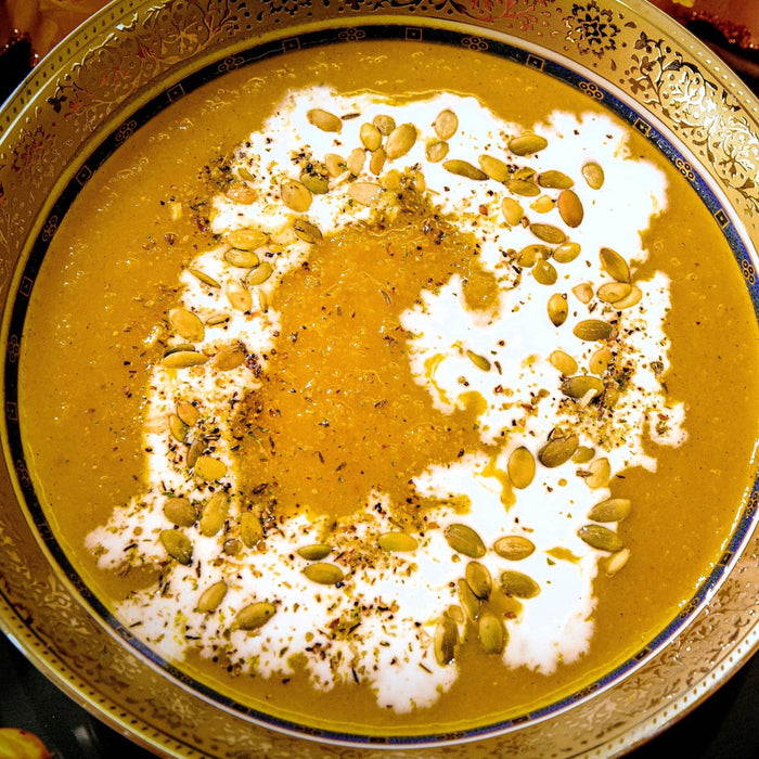A bowl of pumpkin soup with cream and pumpkin seeds.