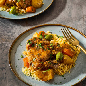 A plate of Moroccan chicken tagine with couscous, carrots, potatoes, and olives, garnished with parsley.
