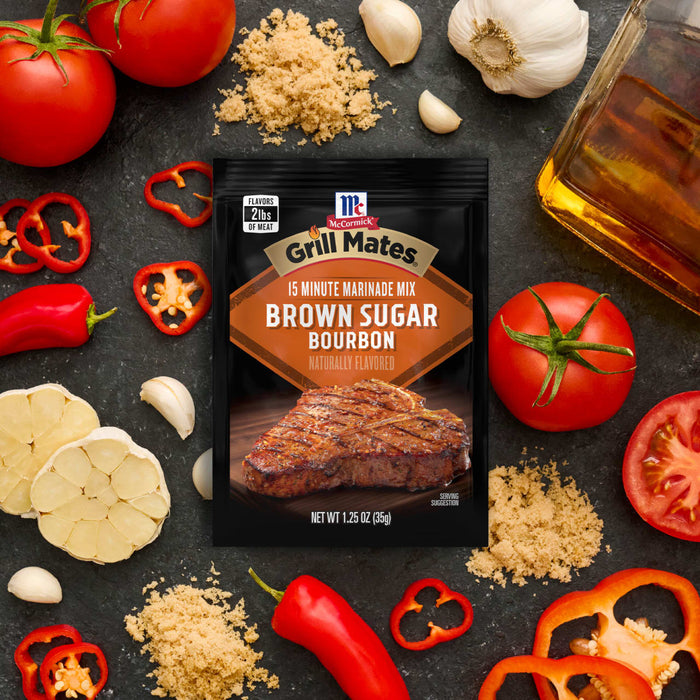 A packet of McCormick Grill Mates Brown Sugar Bourbon seasoning is displayed amidst fresh ingredients like tomatoes, garlic, peppers, and brown sugar, suggesting a flavorful grilling experience.