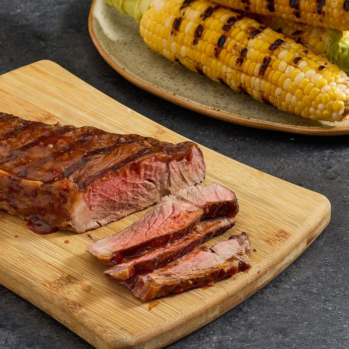 A grilled steak sliced on a wooden board, served with grilled corn on the cob.