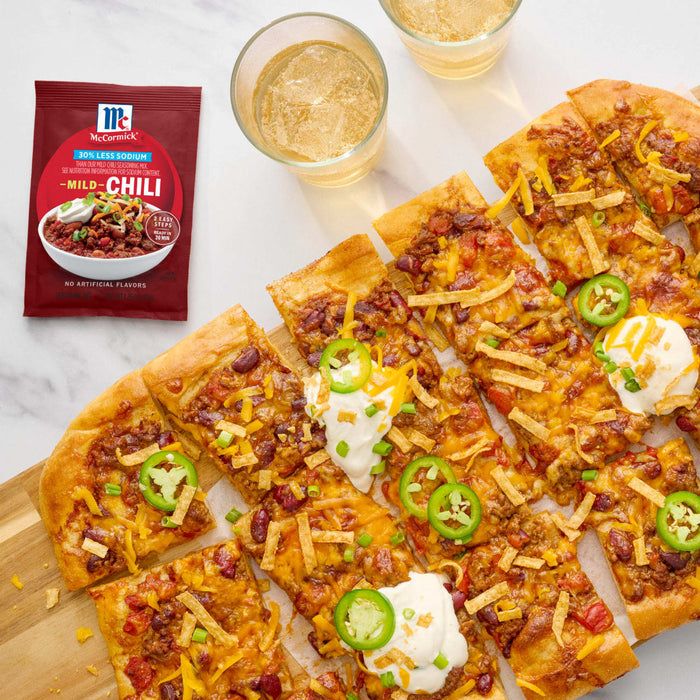 A flatbread pizza topped with chili, cheese, jalapenos, and sour cream, alongside a packet of McCormick Chili seasoning.
