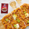 A flatbread pizza topped with chili, cheese, jalapenos, and sour cream, alongside a packet of McCormick Chili seasoning.