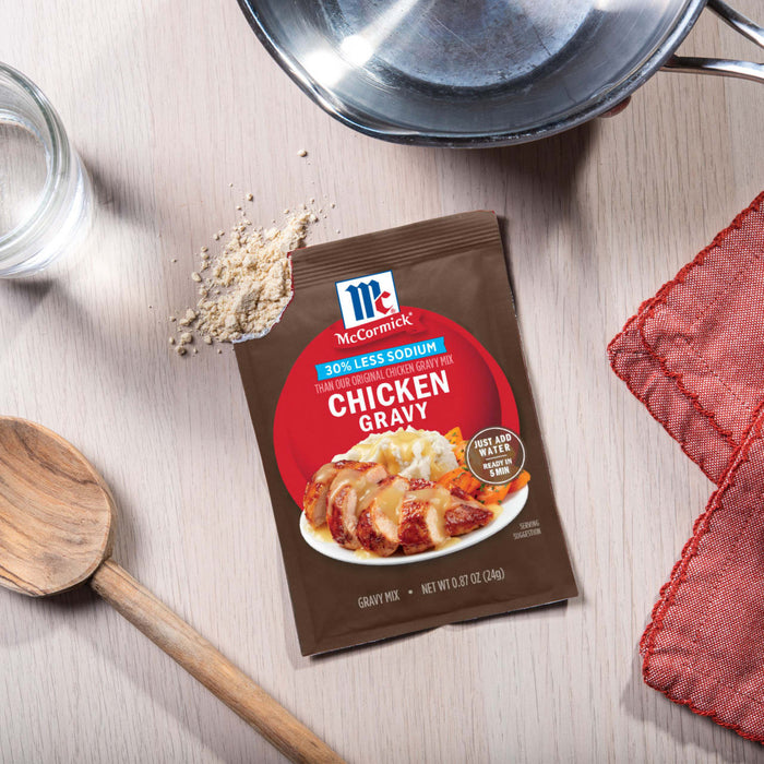 A packet of McCormick Chicken Gravy mix sits on a table next to a wooden spoon and a pot, suggesting a home-cooked meal.