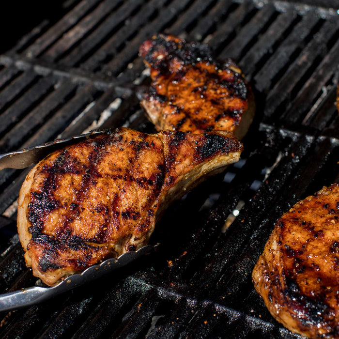 Grilled pork chops with visible grill marks being cooked on a barbecue.