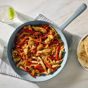 A skillet of chicken fajita ingredients with a package of McCormick Fajita seasoning mix and a finished fajita on a plate.